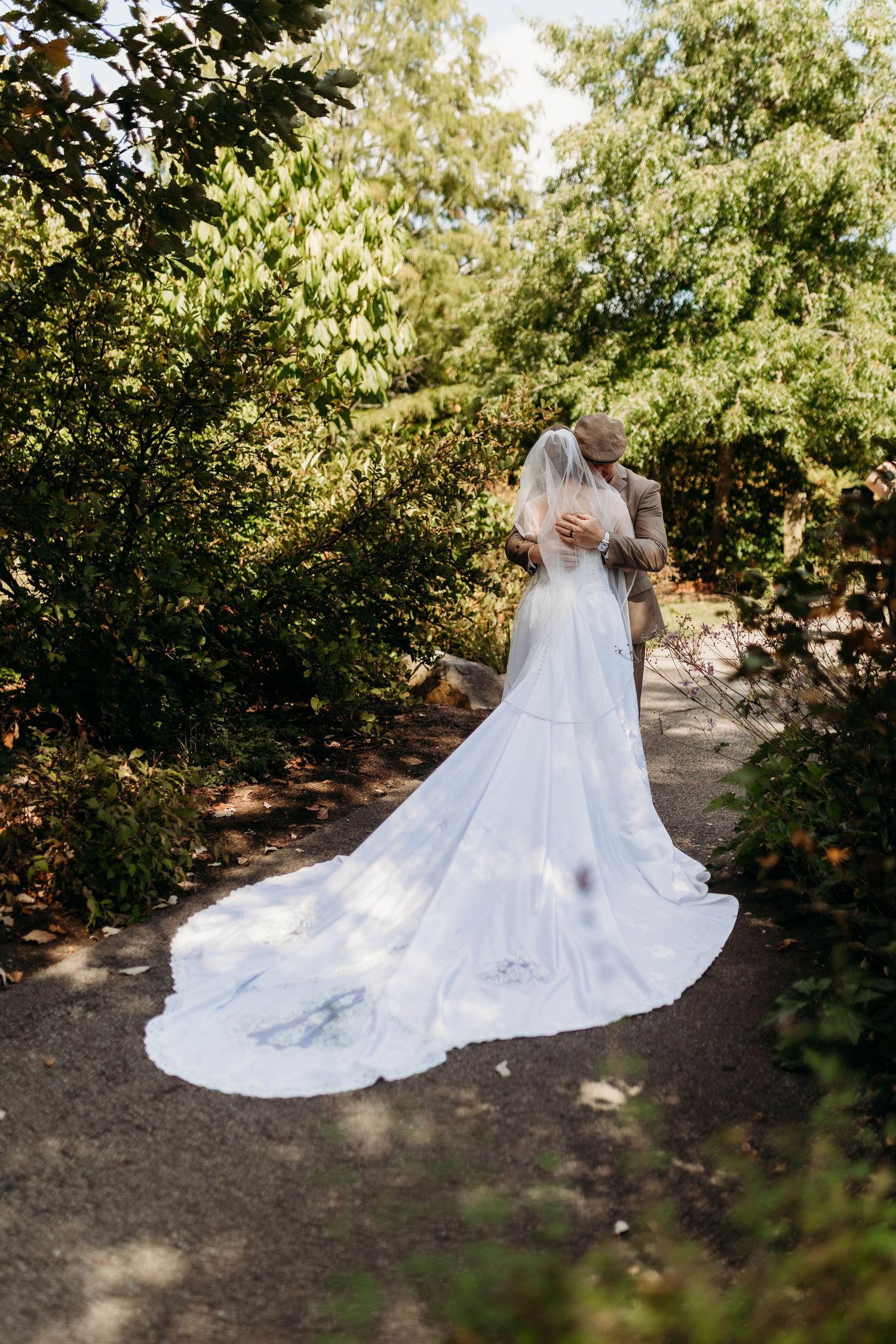 Bride and groom sharing a kiss on a garden path, wedding veil trailing along the ground.