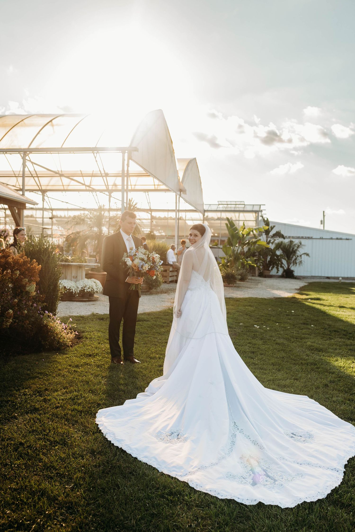 Bride and groom share golden hour moment outdoors with stunning cathedral train spread across green grass.