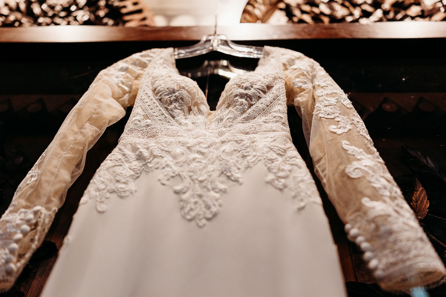 Elegant long-sleeve lace wedding dress hanging on display with intricate floral embroidery and V-neckline.