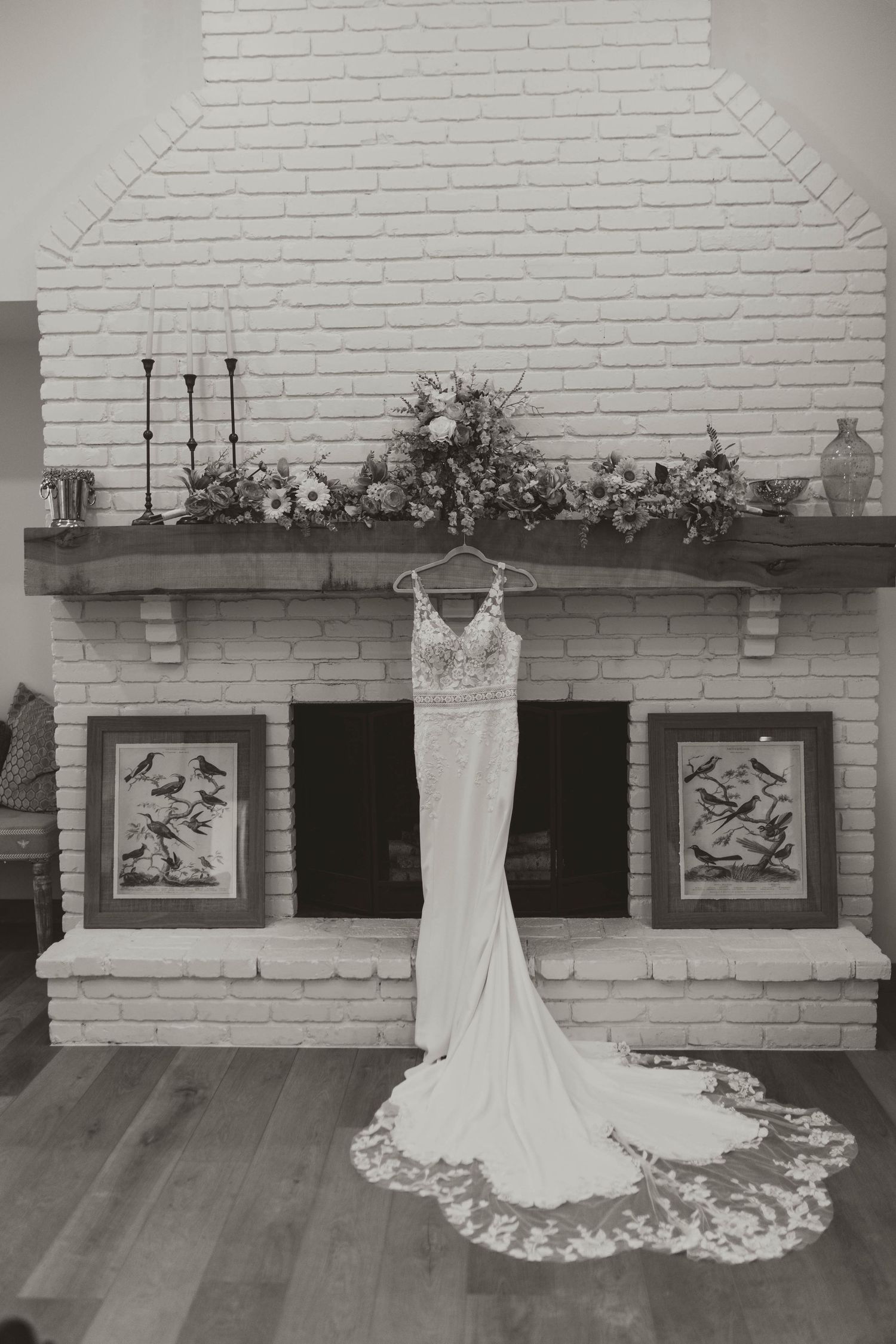 Elegant lace wedding gown with cathedral train hanging over fireplace in black and white bridal photo.