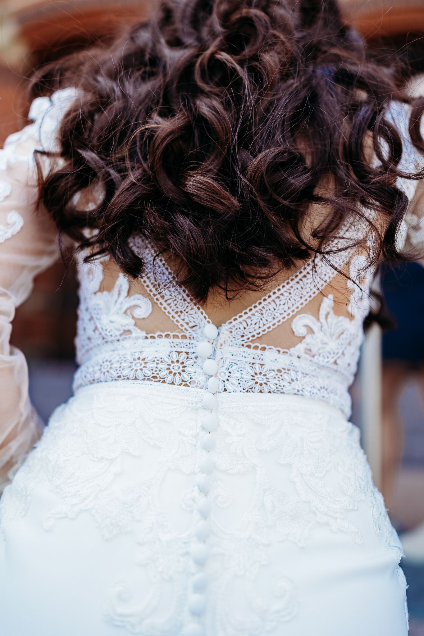Back view of bride in lace wedding gown with button closure and curly updo hairstyle.