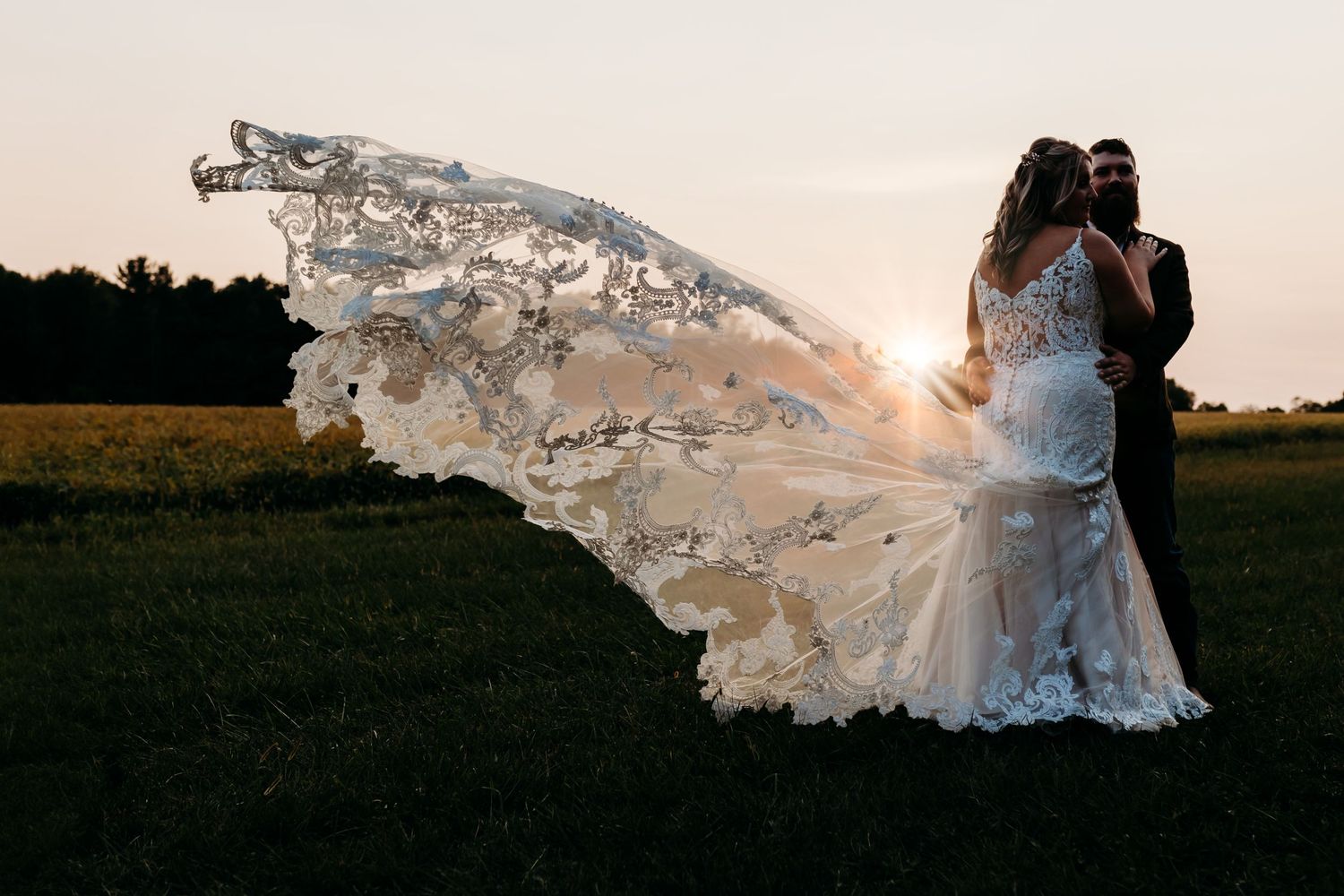 Couple kissing at golden hour as the bride's lace cathedral veil flows in the breeze.