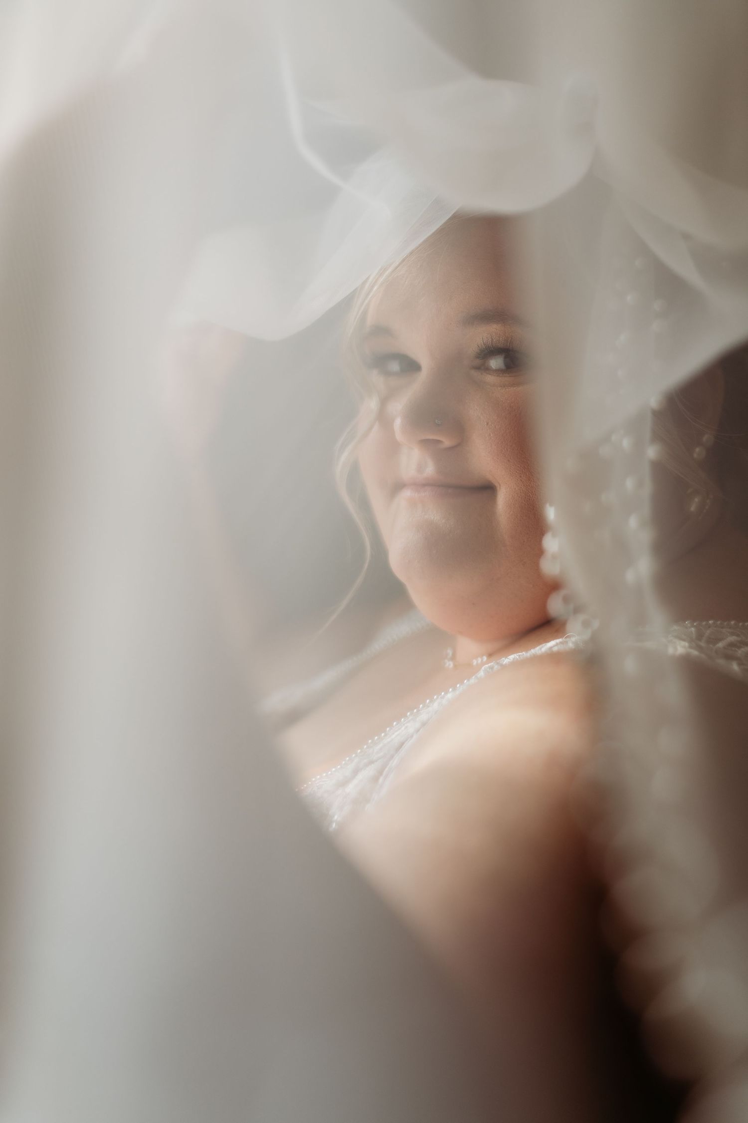 Dreamy soft-focus portrait of smiling bride seen through layers of flowing white wedding veil.