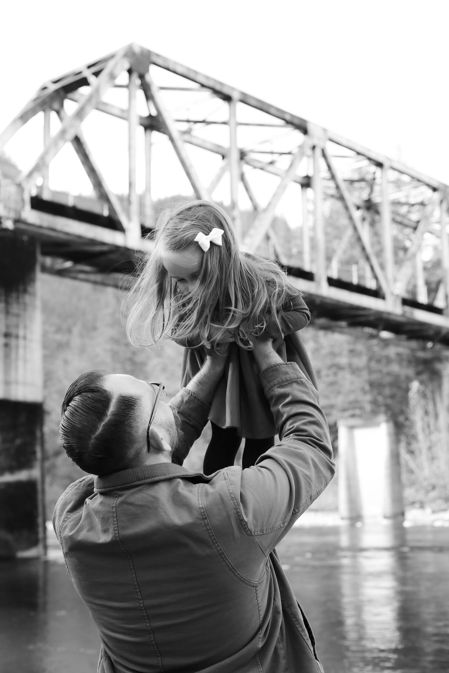 Parent lifting child by bridge in dramatic black and white photography.