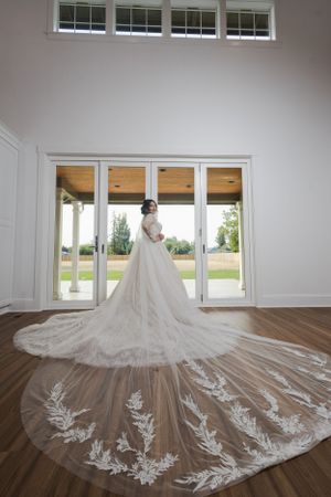 A dramatic wedding dress with intricate lace train displayed in front of large windows with natural lighting.