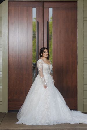 Full-length portrait of a bride in a white lace gown against modern wooden doors.