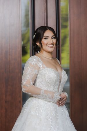 A bride in an elegant lace wedding gown poses against a wooden door.