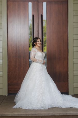 A bride in a full lace wedding gown with train poses by wooden doors.