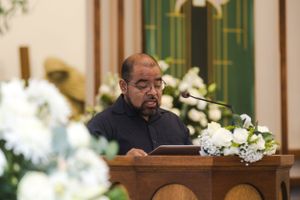 A speaker at a church podium with white floral decorations.