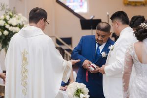 A wedding ceremony showing the exchange of rings with a priest in white robes.