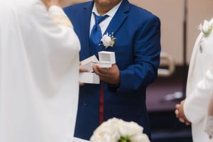 Close-up of hands exchanging rings during a wedding ceremony with a blue suit visible.