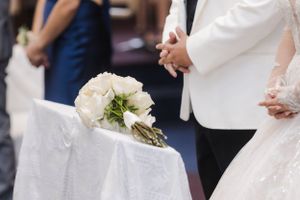A white bridal bouquet rests on a cloth-covered surface during a wedding ceremony.