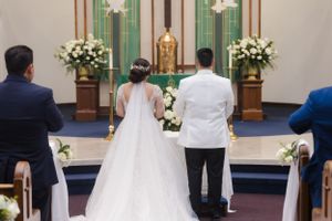 Wedding ceremony in progress at church altar decorated with white floral arrangements.
