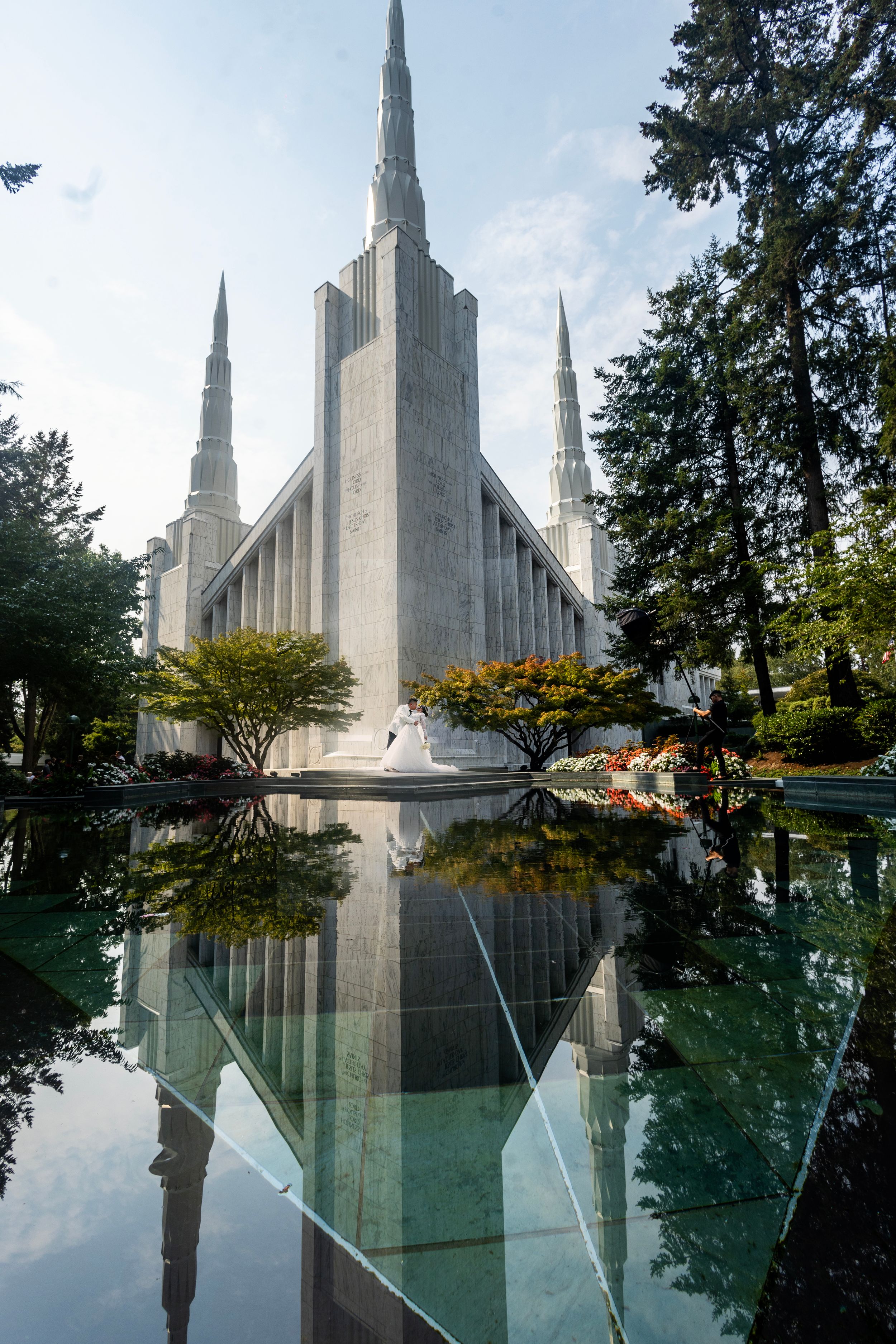 A modern white temple building reflected in a pool with dramatic spires against a blue sky.