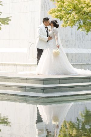Bride and groom share an intimate moment on marble steps with their reflection in water below.