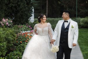A wedding couple walks together on a garden path surrounded by blooming flowers and greenery.