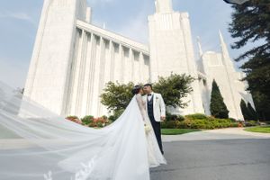 A dramatic wedding photo in front of a grand white temple with flowing veil in the foreground.