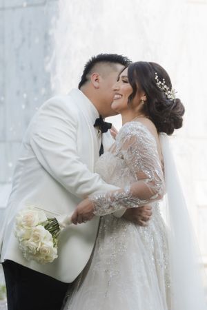 A joyful wedding couple embraces while holding a bouquet of white roses.