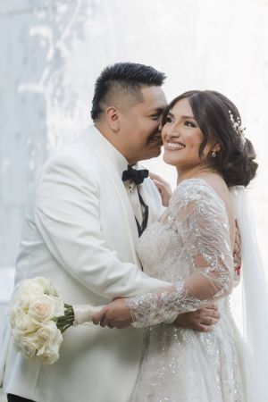 A candid wedding moment captured as the couple shares laughter while holding a white rose bouquet.