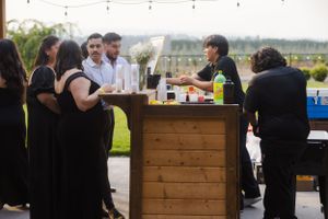An outdoor wedding reception setup with wooden bar and string lighting.