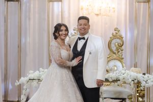 Newlyweds pose elegantly in front of ornate gold decor and white floral arrangements.