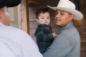 Person in cowboy hat holding small child at formal event.