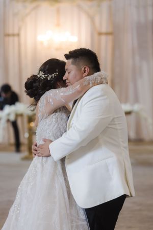 Couple sharing an intimate dance moment in white formal attire.