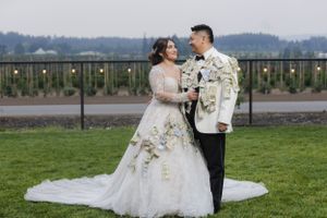 A romantic wedding portrait taken outdoors with string lights and natural scenery in the background.
