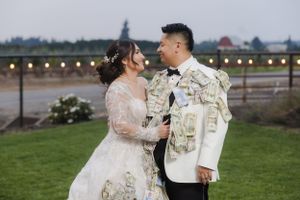 An outdoor wedding portrait features a couple against a backdrop of mountains and twinkling lights.