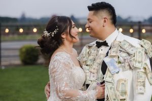 A romantic wedding photo captures a couple outdoors with mountains and string lights in view.