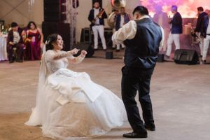 Wedding guests dance and celebrate on a dimly lit dance floor with pink and purple lighting effects.
