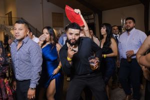 Large group of wedding guests dancing together at dimly lit reception venue.