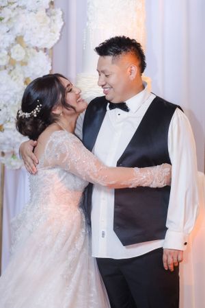 Tender moment between newlyweds sharing laughter against floral backdrop.