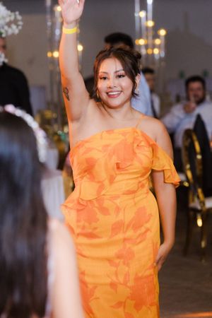 Wedding guest in vibrant orange ruffled dress dances joyfully at reception celebration.