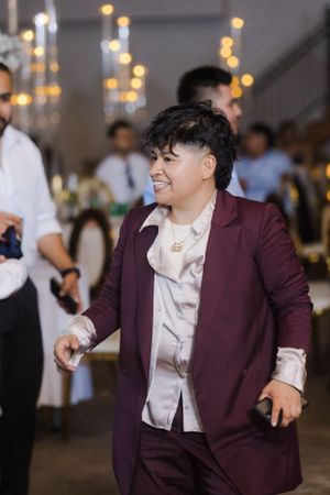 Guest in burgundy blazer and white shirt dances energetically at wedding reception.