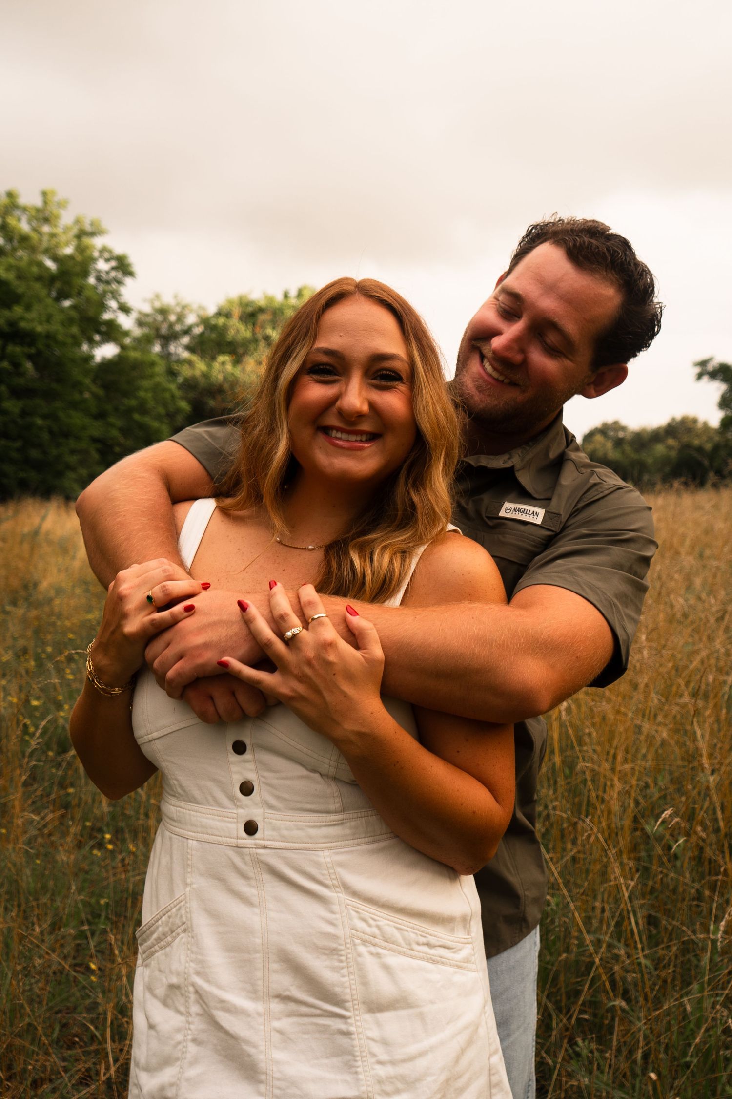 A couple embraces and laughs together in a golden field during sunset.
