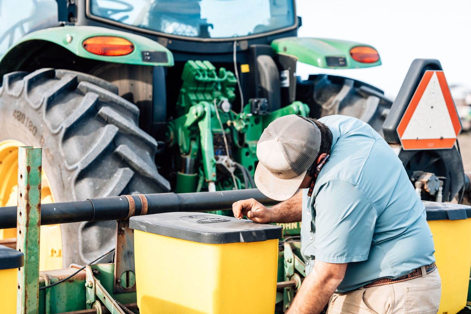 Agricultural worker preparing equipment and supplies on a large green tractor.