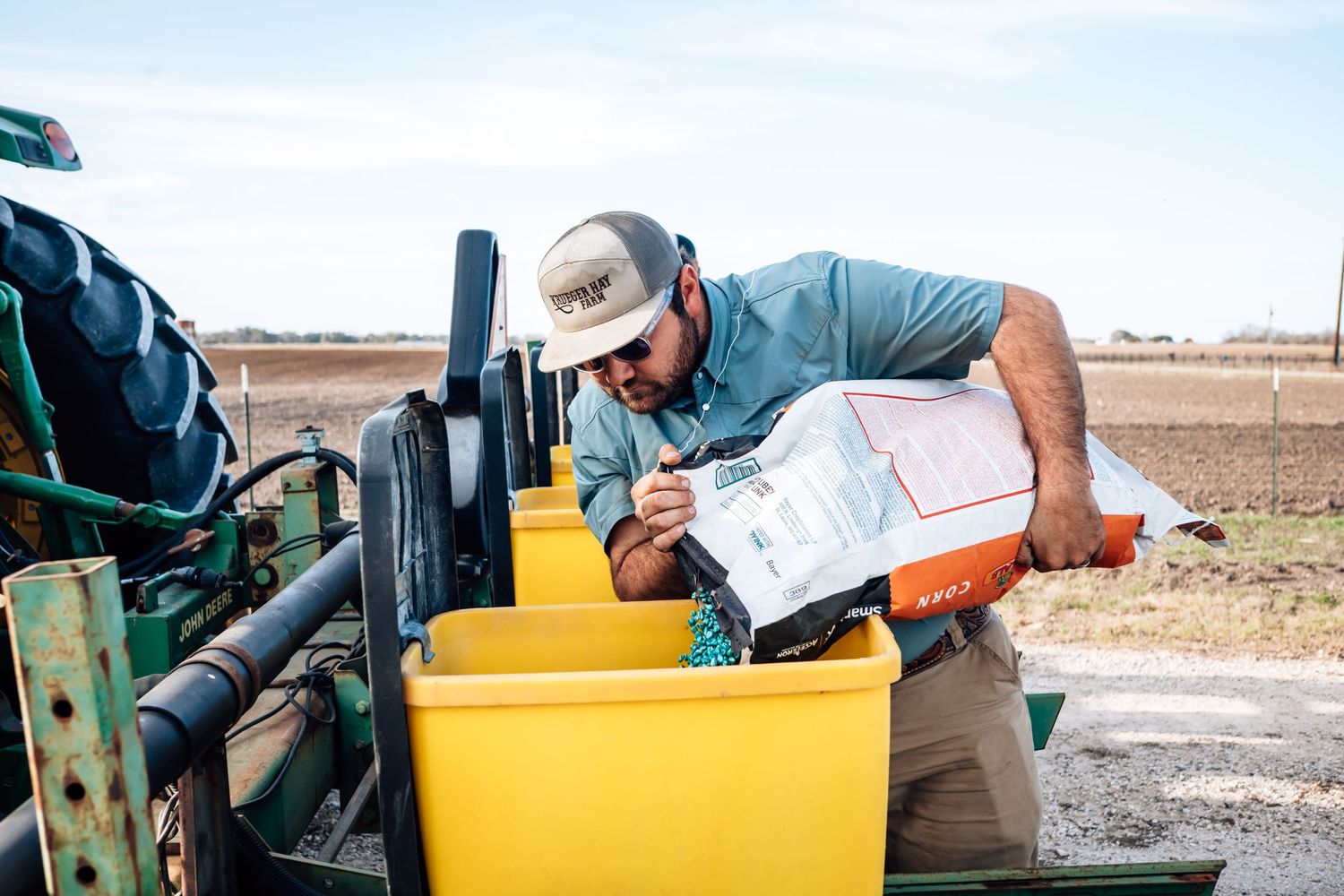 Farm worker carefully measuring and pouring materials into yellow equipment containers.