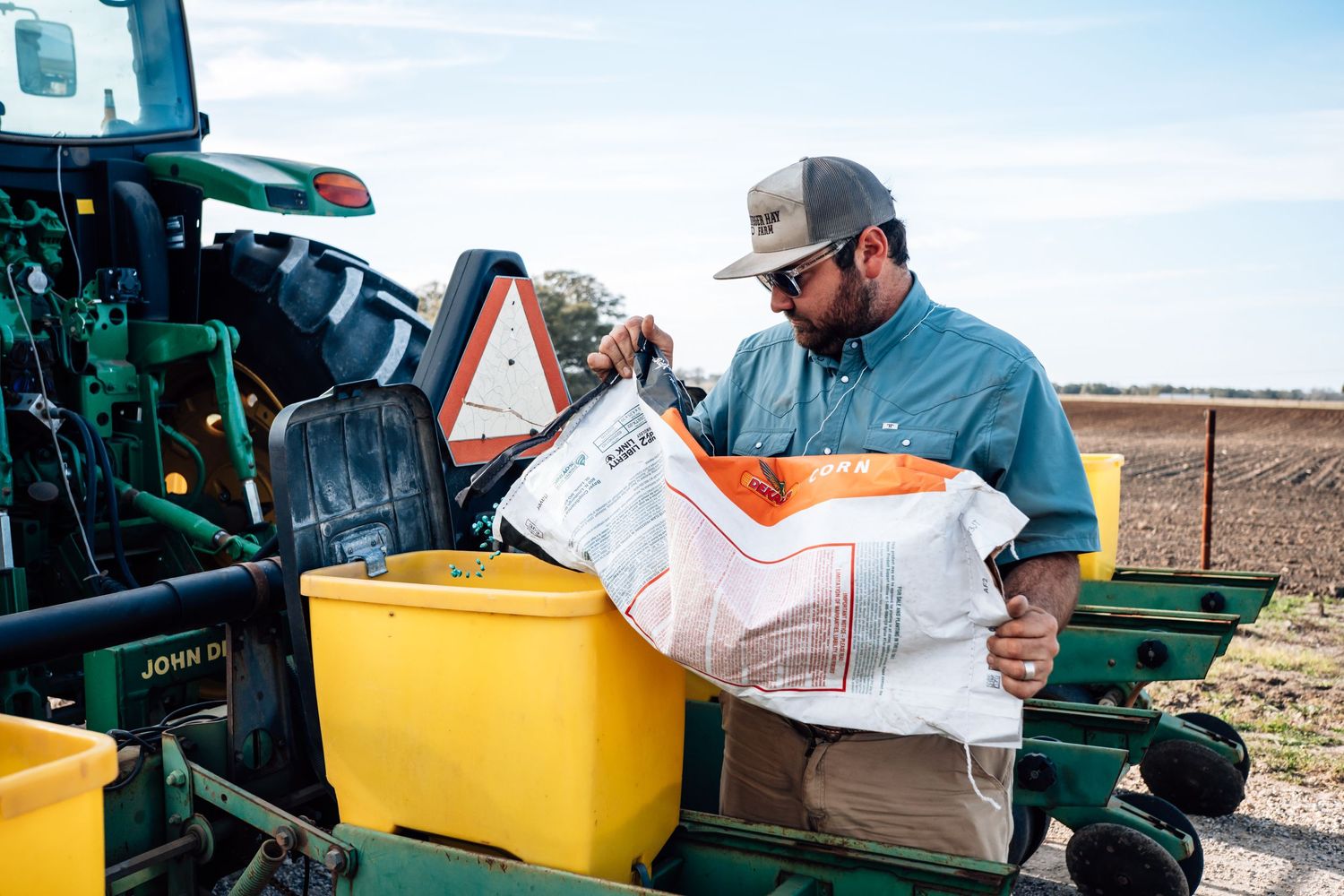 Farmer loading agricultural supplies into yellow equipment containers on a tractor.