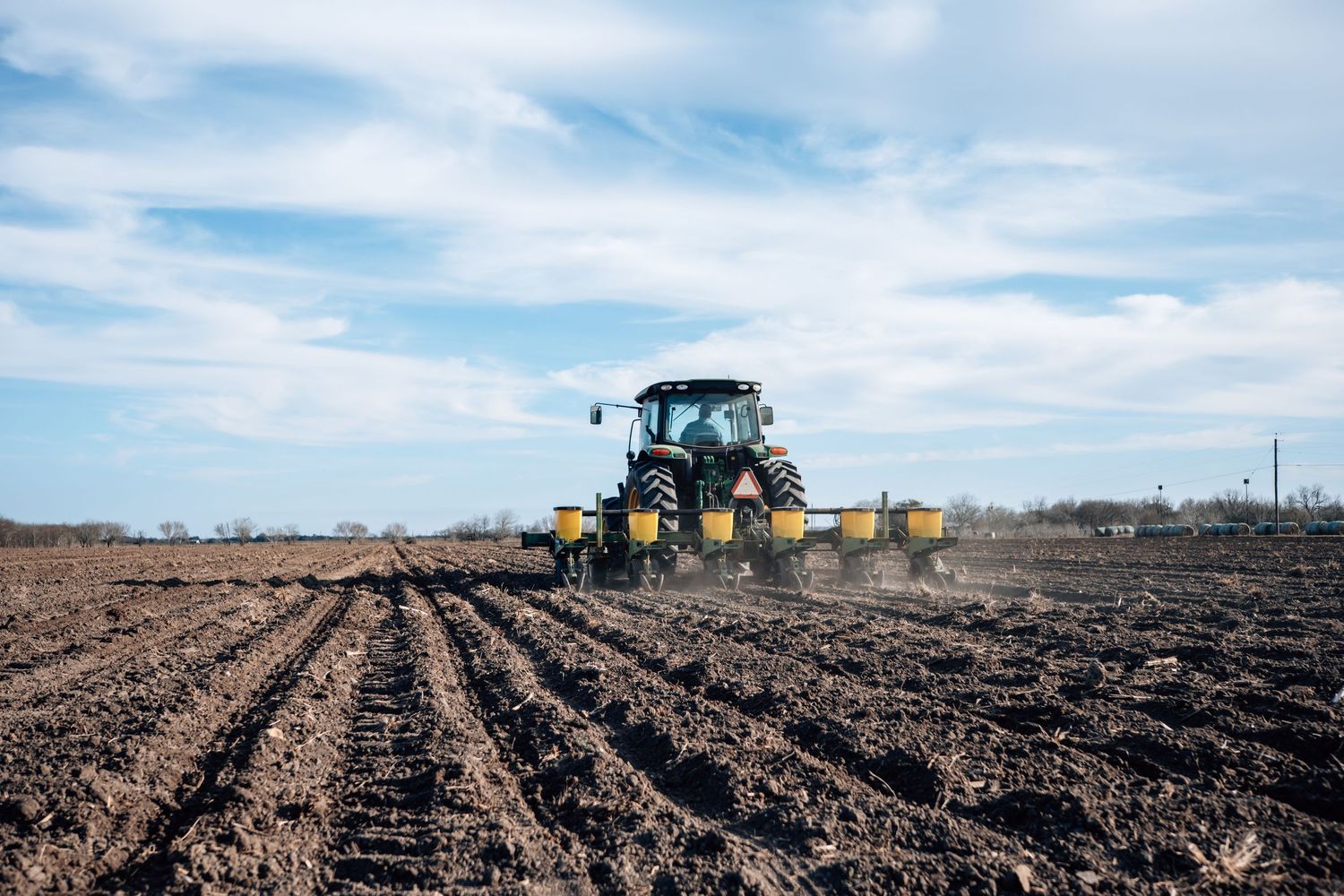 A yellow tractor plowing rows in a freshly tilled agricultural field under blue skies.