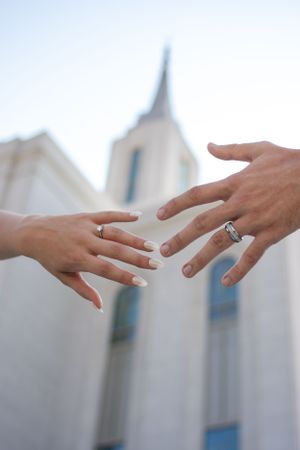Bride and groom reach out to each out with Orem, Utah temple in background.