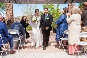 Bride and groom walk hand in hand down the aisle on their wedding day towards camera at their garden venue in Salt Lake City, Utah.
