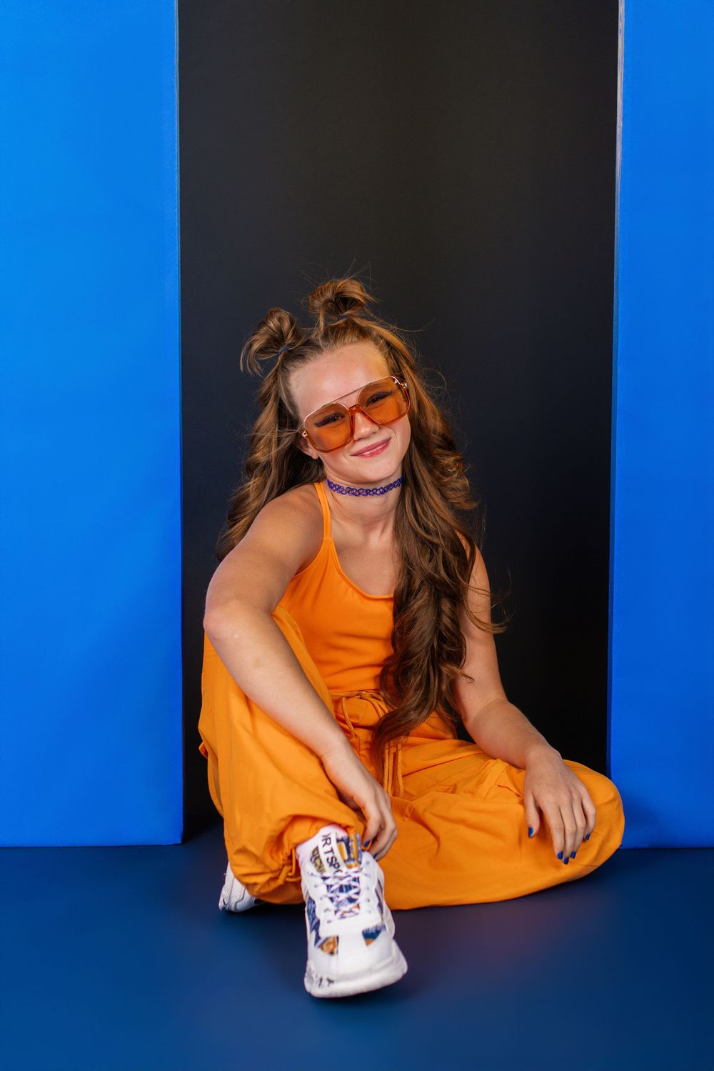 Casual fashion shoot with orange dress against blue and black backdrop.