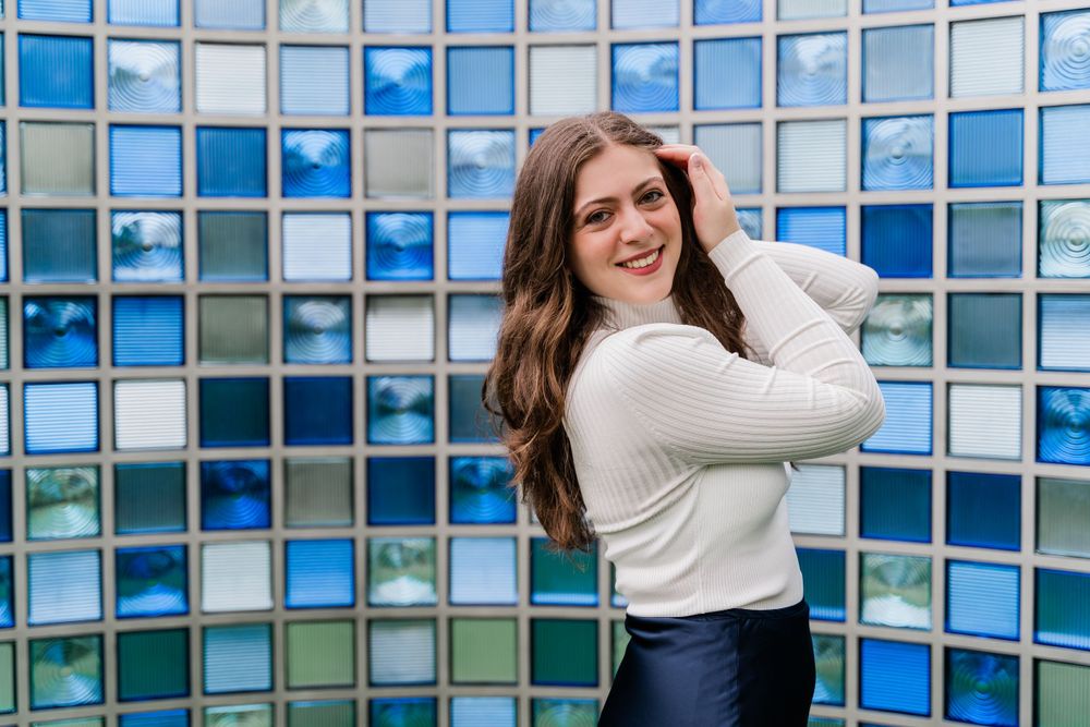 Casual fashion pose against blue and white mosaic tile wall featuring a white turtleneck sweater.