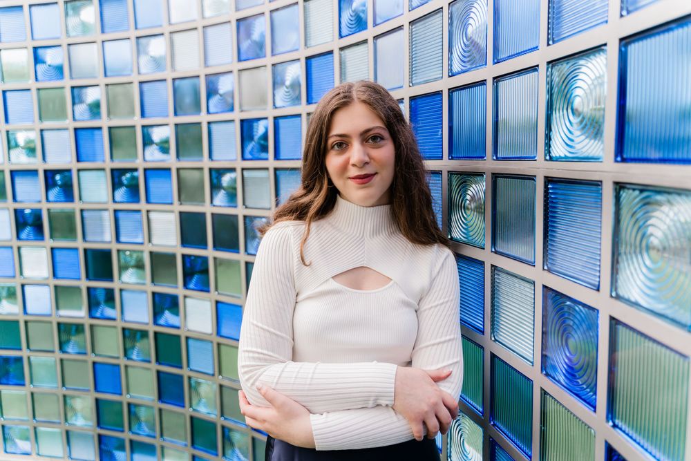 Fashion portrait against a blue mosaic wall featuring a white sweater with geometric cutout detail.
