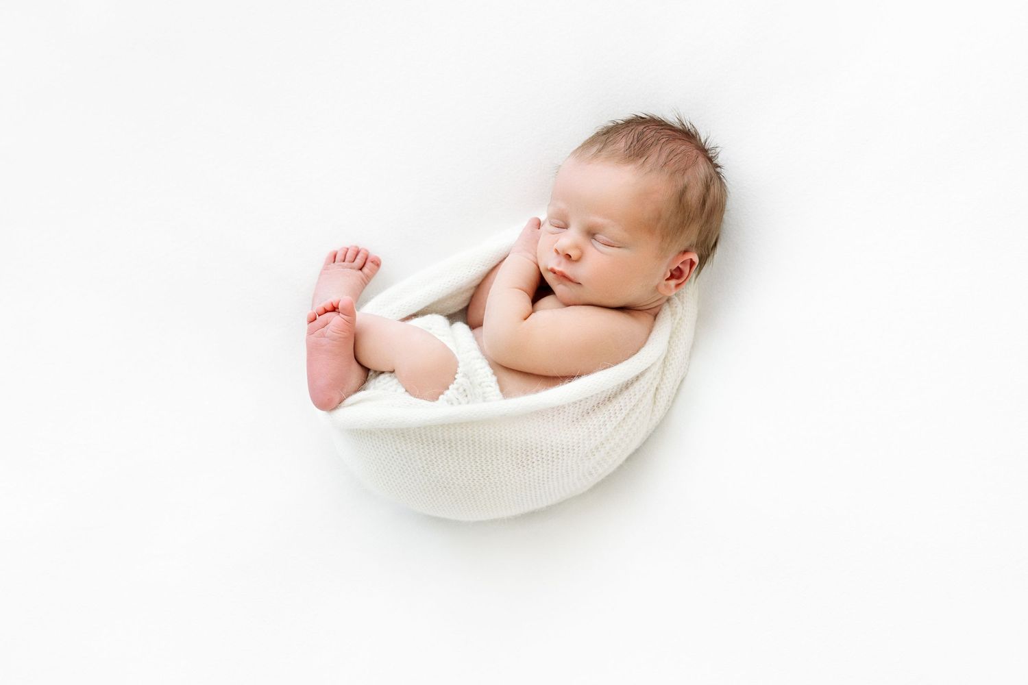 Cozy newborn boy, artfully wrapped in minimal white photo setup