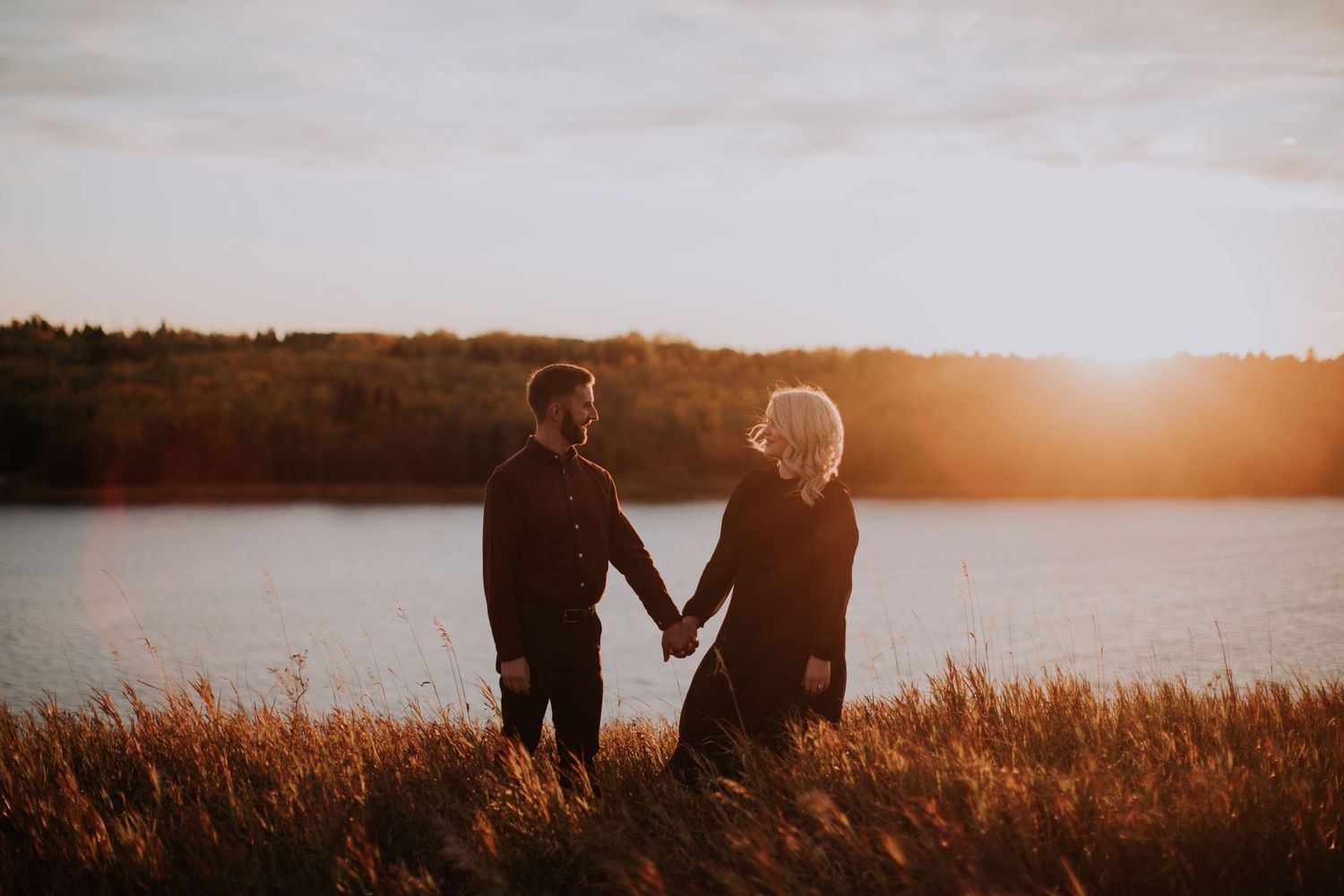 A couple holds hands while watching a golden sunset by a serene lake.