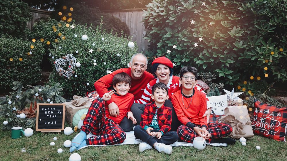 A festive holiday photo setup with red plaid blankets, pillows and Christmas decorations in a garden setting.