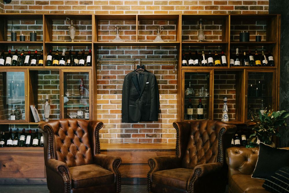 Vintage lounge area with leather chairs and wooden display shelves against exposed brick wall.