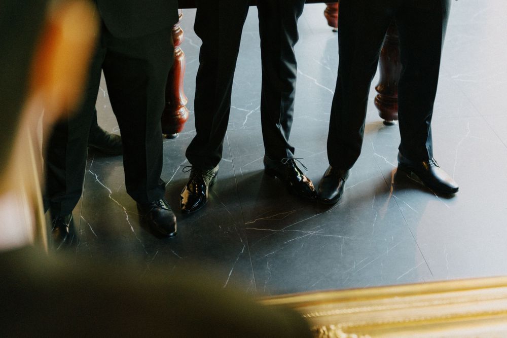 Low angle view of formal black shoes and pant legs on dark floor.